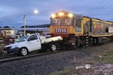 A freight train stopped on the tracks with a white ute on the tracks in front of it.