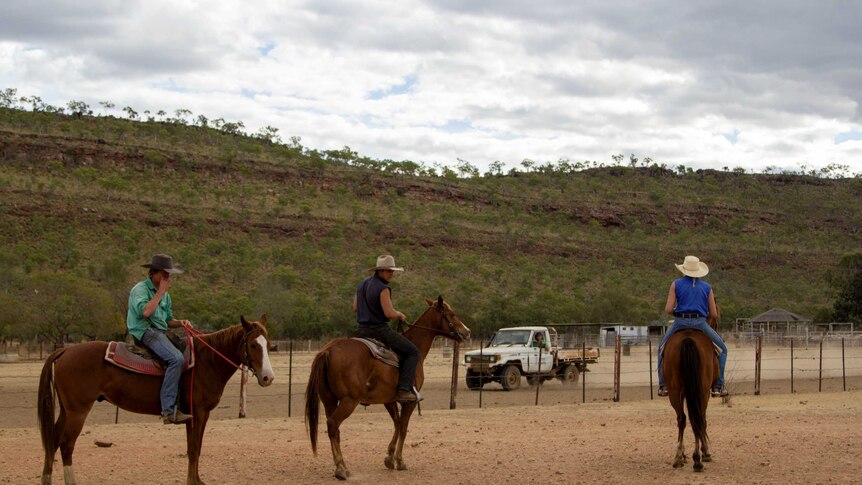 three people on horseback with a range in the background.