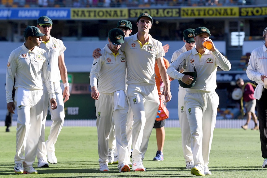 Australian cricketers walk off the field at the Gabba. Pat Cummins has his arm around Travis Head.