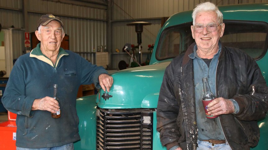 Ray Miguel and Bruce Ingleton lean on a vintage car inside the men's shed