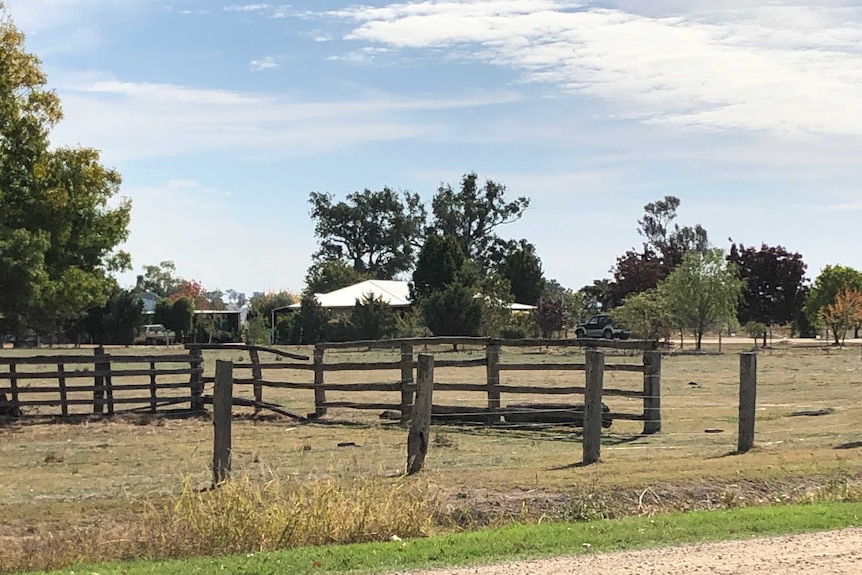 Wooden posts and wire fencing runs along a rural property viewed from a gravel road.