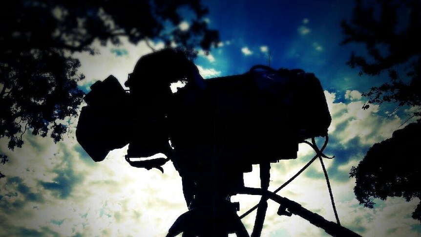 Silhouette of camera with blue sky and clouds in background