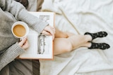 A girl reading a book and having a coffee.