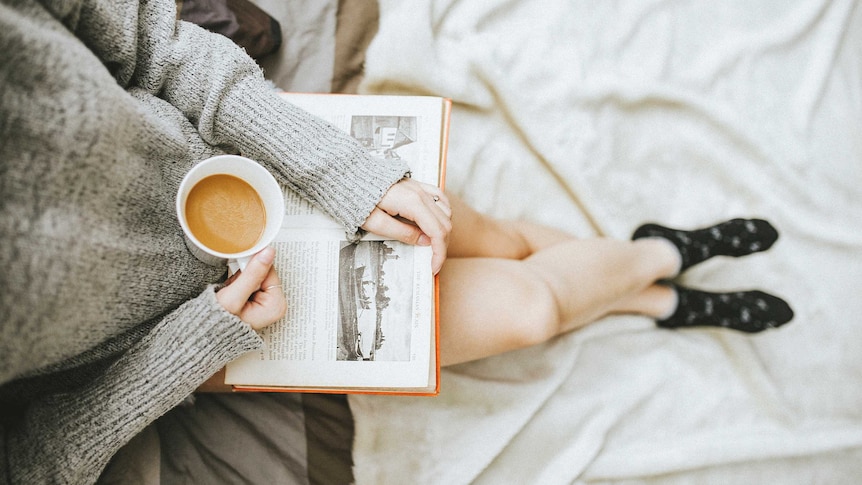 A girl reading a book and having a coffee.