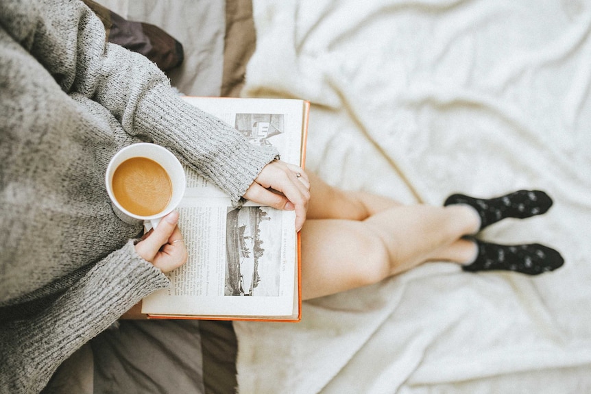 A girl reading a book and having a coffee.