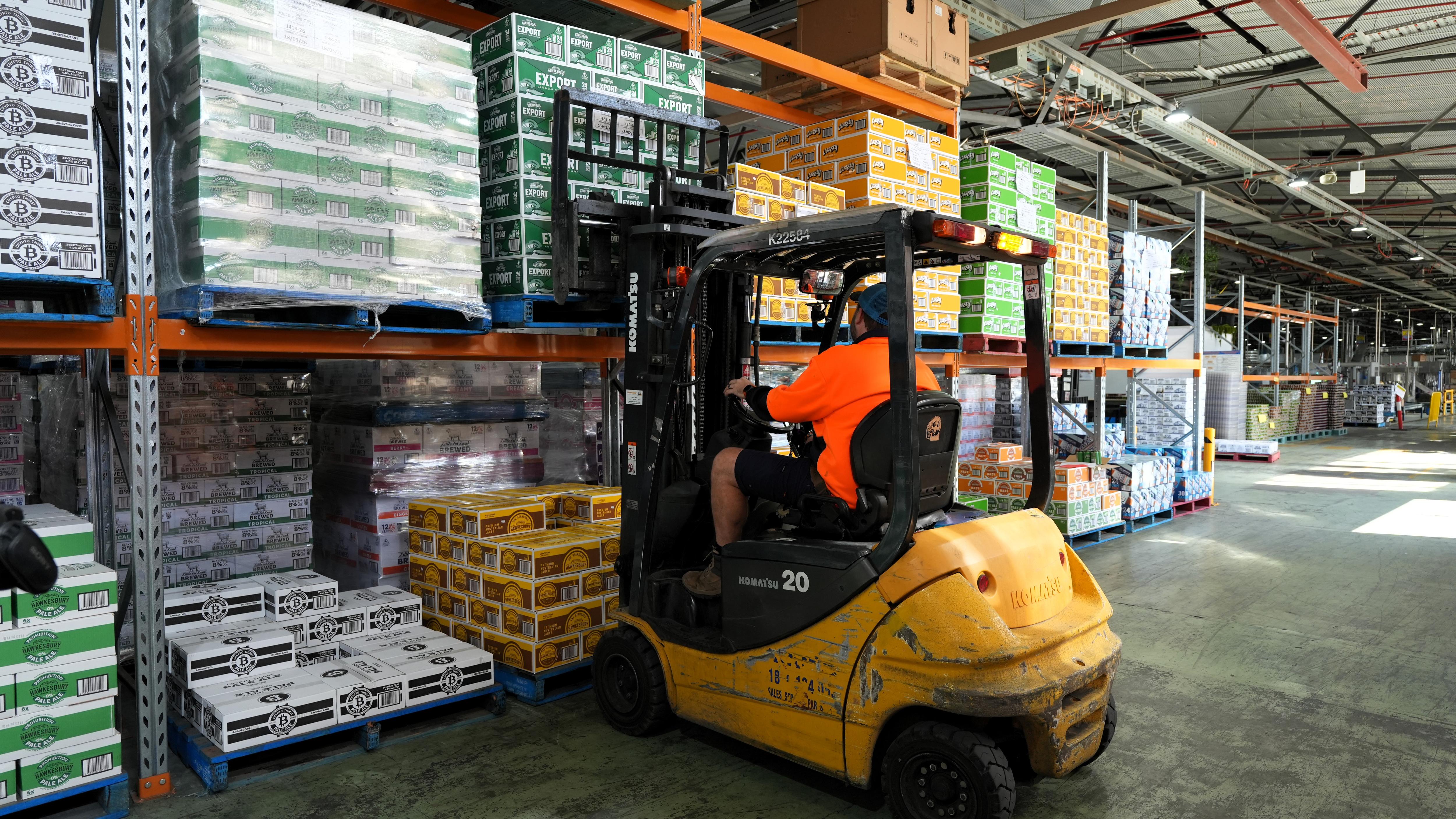 Colourful cardboard cases of beer stacked on shelves. A forklift is moving one pallet load.