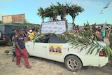 Two supporters smile under a thatched shelter sticking out of an Andrew Mald campaign car.