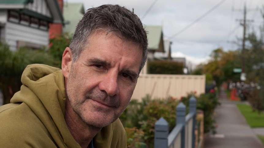 A man in a hooded jumper leans over a front yard fence