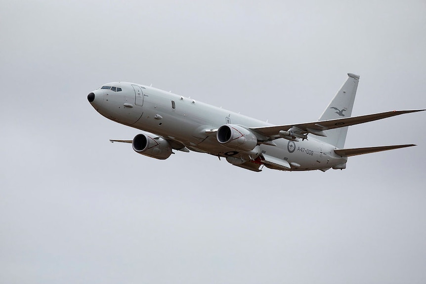 A grey military aircraft flies against a cloudy sky
