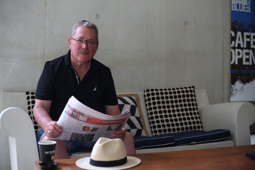 Retired prison officer Peter Gow sits at a cafe in Brisbane and reads the paper
