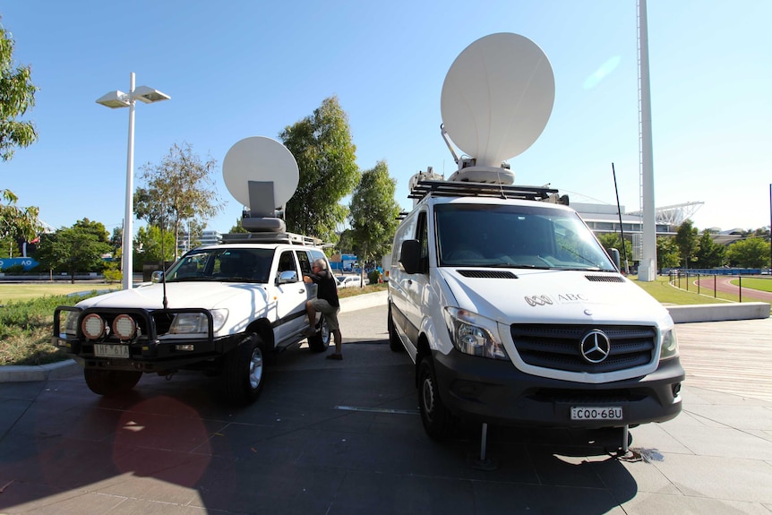 Two links vans with satellite dishes up parked with sporting stadium in background.