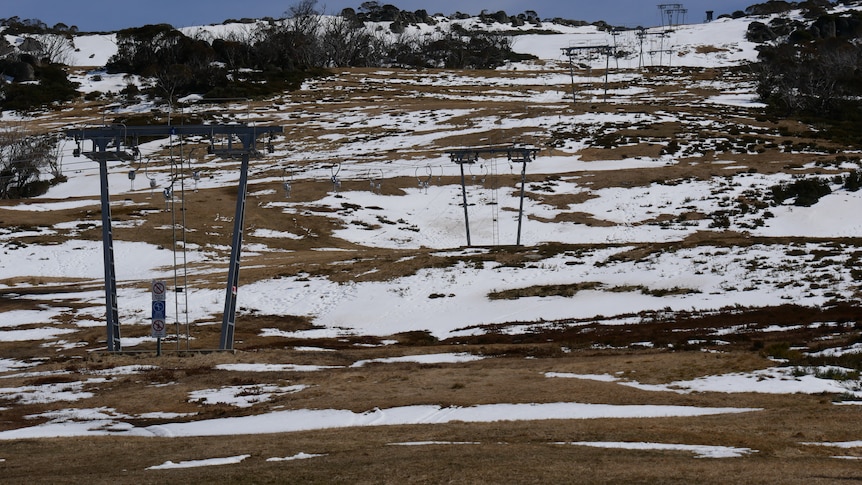 a hillside covered in patchy snow with a closed chair lift