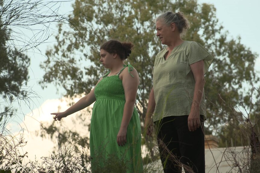 Una mujer con un vestido verde señala a lo lejos, otra mujer mira hacia donde ella señala.