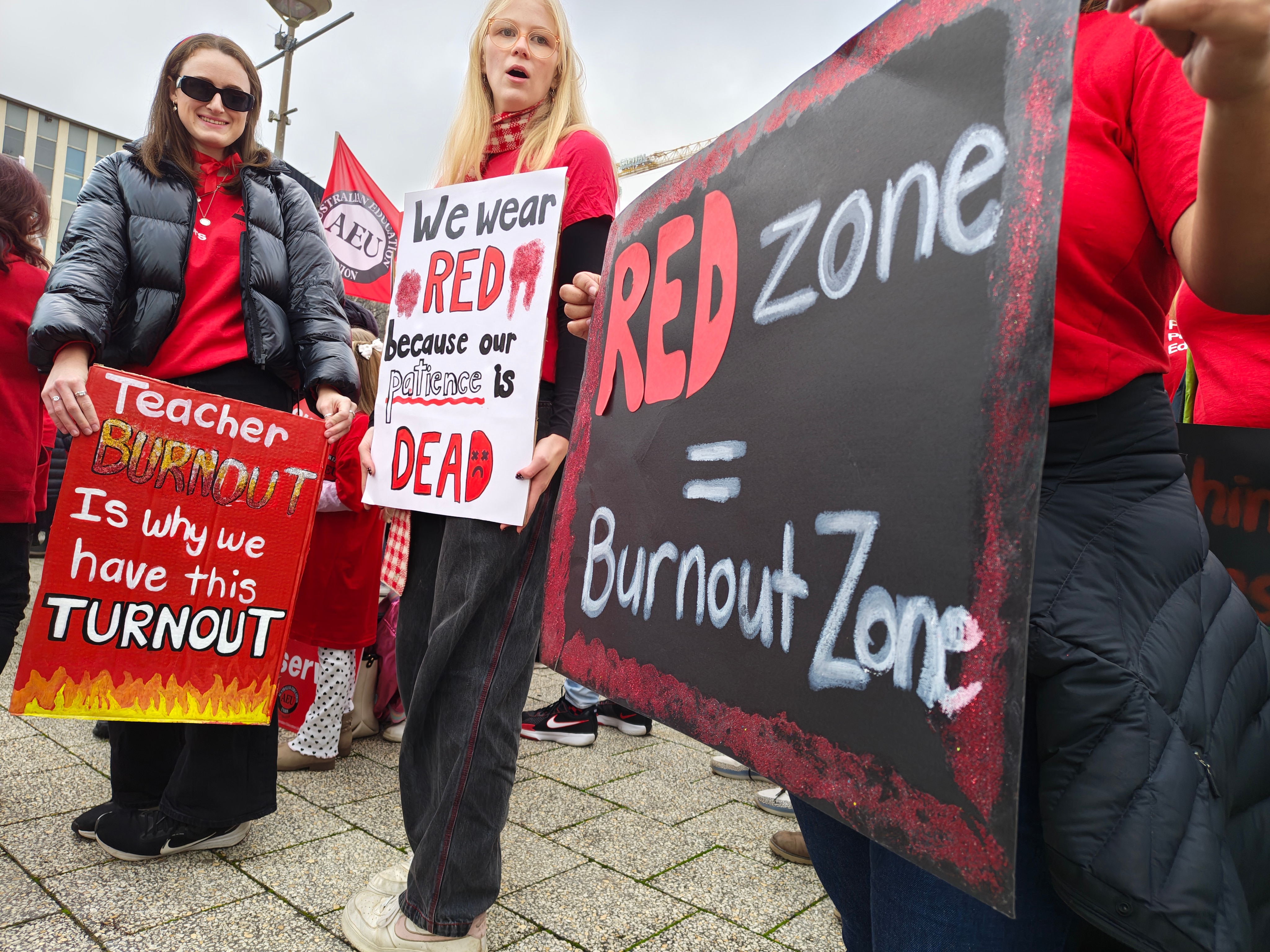 People stand wearing red and holding protest signs.
