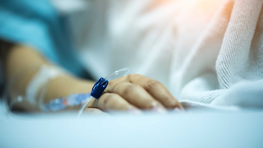 Person's hand rests on hospital bed.