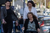 A woman in a wheelchair accompanied by two younger women on a sidewalk.