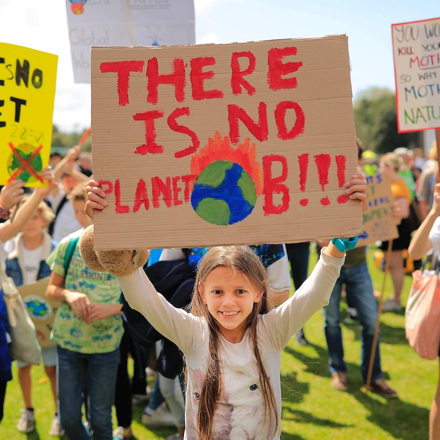 A young girl holds a hand made sign reading 'There is no planet B'.