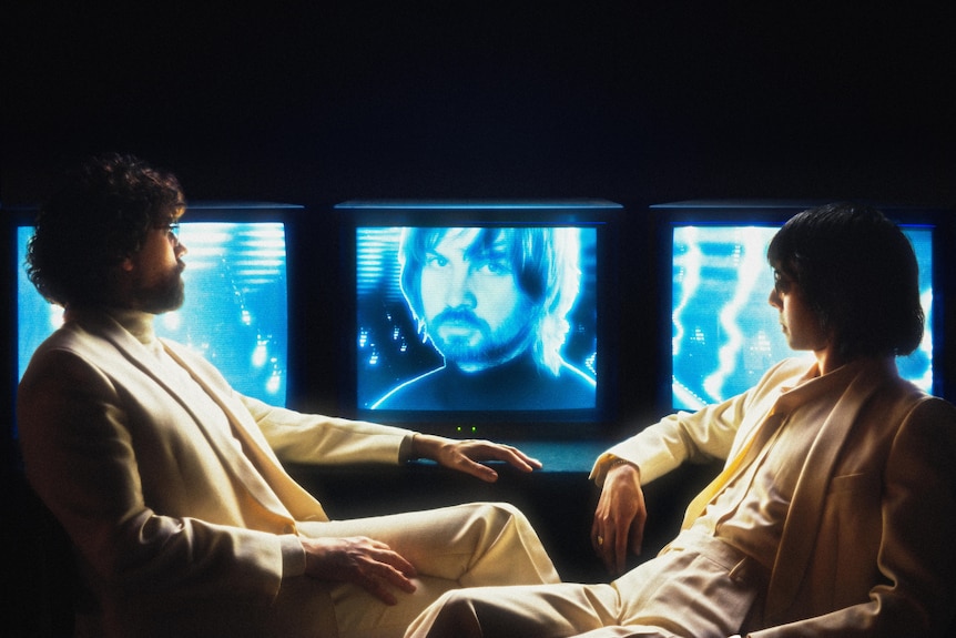 Justice's Gaspard Augé and Xavier de Rosnay sit looking at a blue TV screen depicting Tame Impala's Kevin Parker
