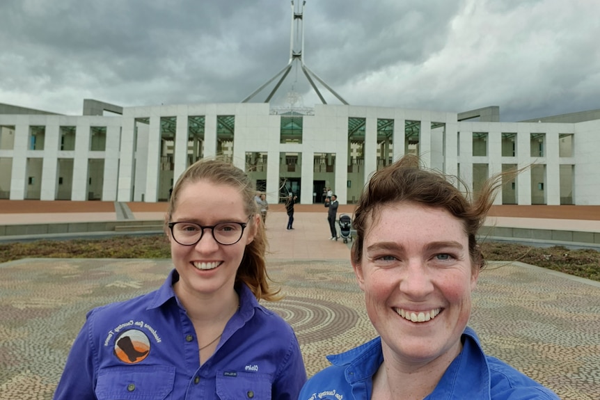 Two women with dark hair take a smiling selfie outside Parliament House.