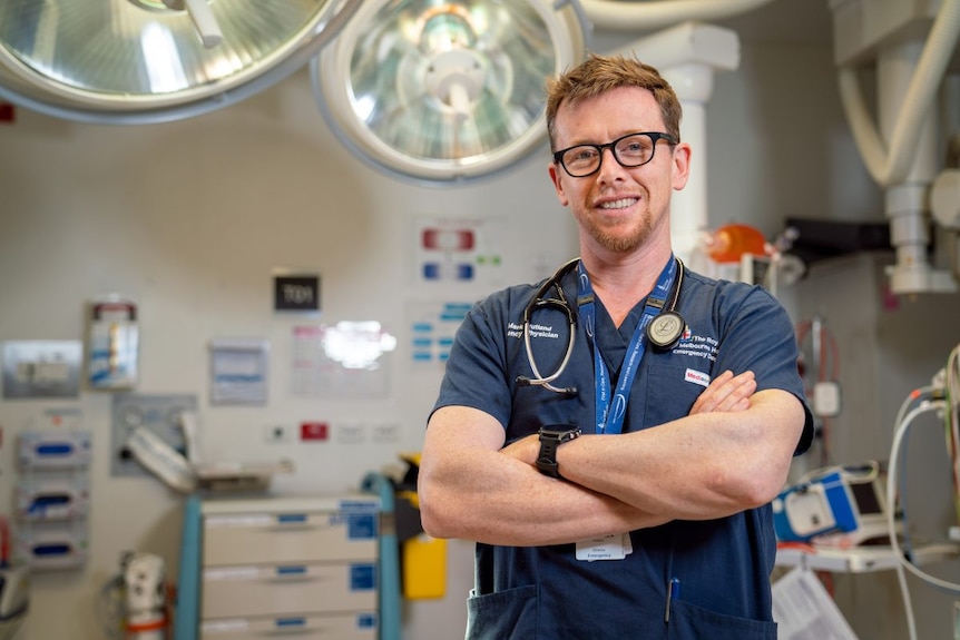 A man with glasses wearing hospital scrubs.