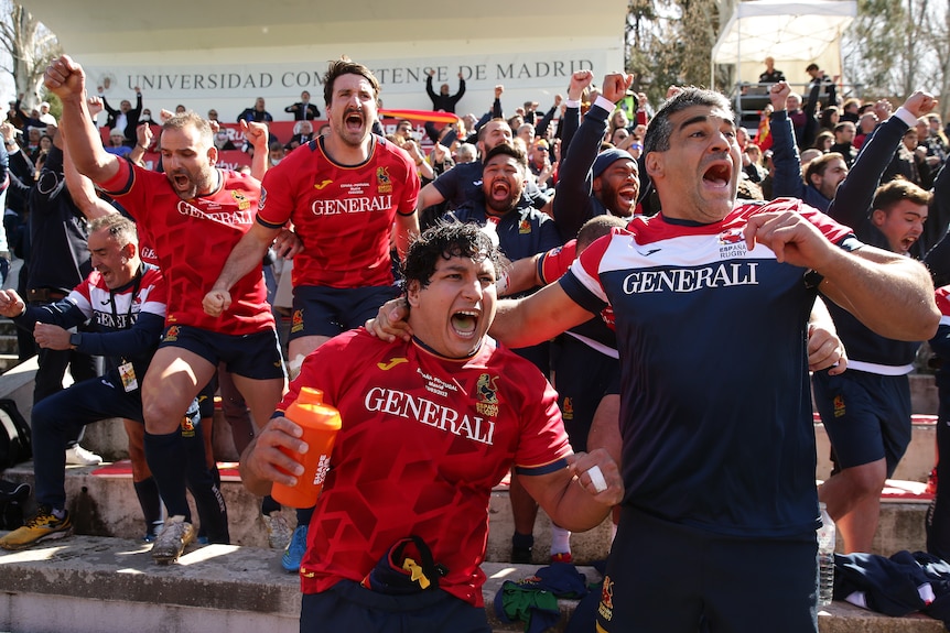 Los jugadores y entrenadores de la unión de rugby saltan de la banca de alegría mientras la multitud celebra en el fondo.