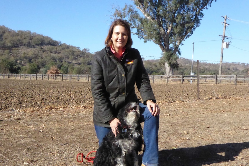 A woman with brown hair standing in a dirt paddock with a black dog.