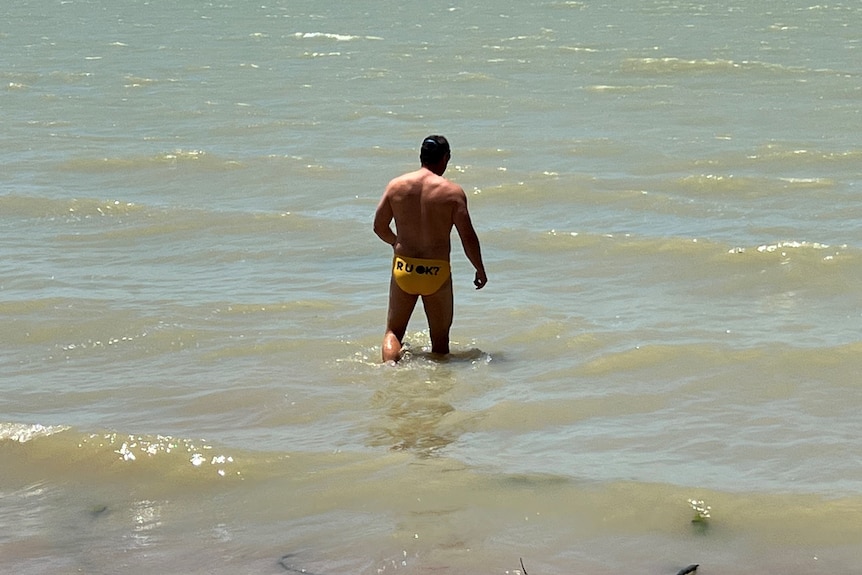 A man wearing yellow swimmers walks into an open body of water
