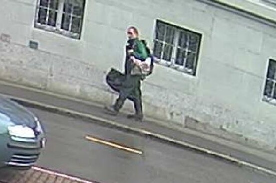 Grainy CCTV footage shows a man carrying two large bags walking down a street.