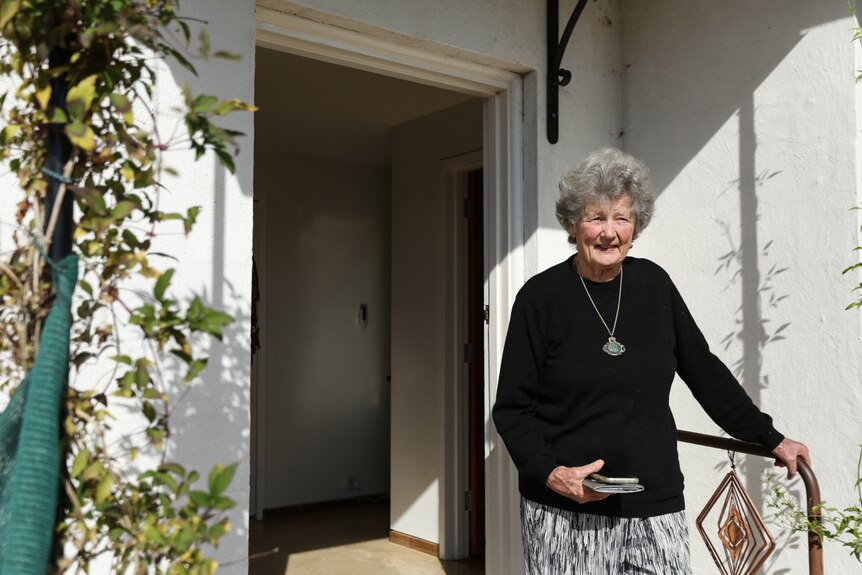 Maggie McLeod standing on her front doorstep against the background of her white home.
