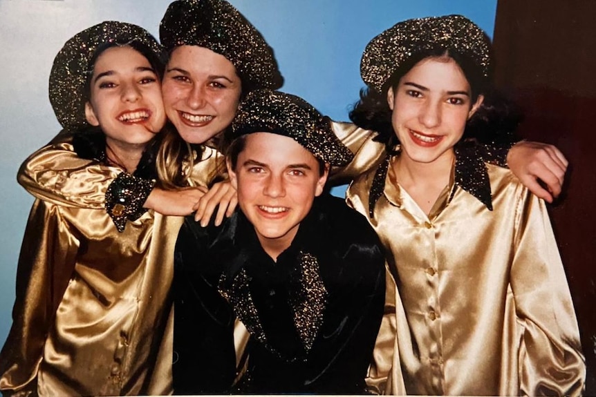 A group of three girls and one boy in matching gold costumes