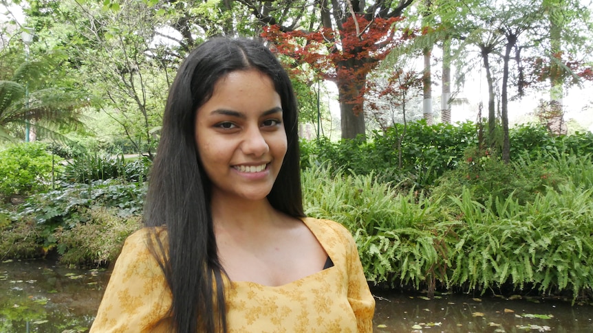 Young woman in yellow top smiling in a garden