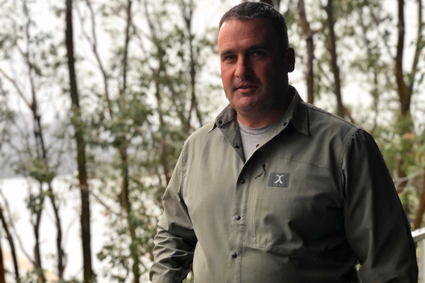 A man in a khaki shirt stands posing for a photo.