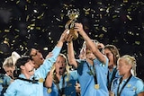 Australia's women's soccer team lifts the Tournament of Nations trophy as confetti falls on them.