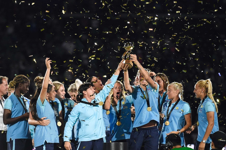 Australia's women's soccer team lifts the Tournament of Nations trophy as confetti falls on them.