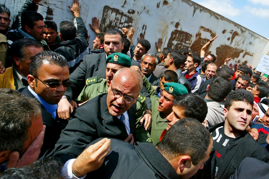 Saeb Erekat clinches his fingers as he moves through a dense crowd of protesters while surrounded by his security detail.