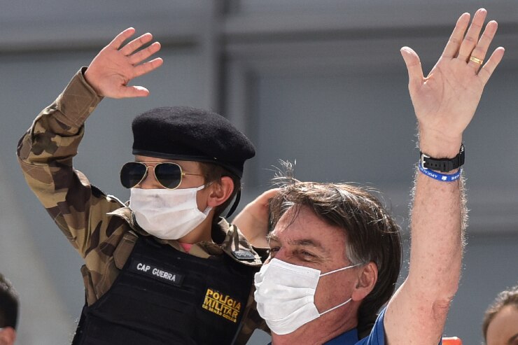 Brazil's President Jair Bolsonaro, wearing a mask against the spread of coronavirus, carries a child.