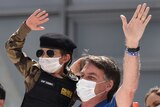 Brazil's President Jair Bolsonaro, wearing a mask against the spread of coronavirus, carries a child.