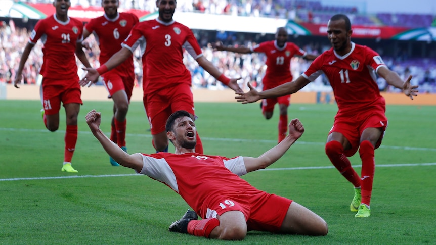 Anas Bani Yaseen slides on his knees with arms aloft as teammates rush in to join him after scoring for Jordan