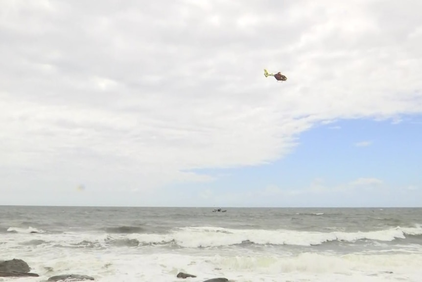 A beach is shown with a chopper in the sky.