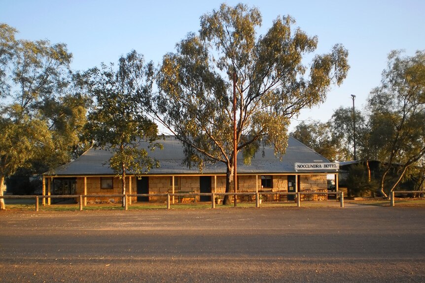 An old sandstone building sits in the shade of some large trees at sunrise