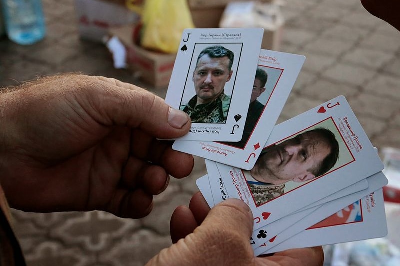 A hand holding several playing cards, one featuring Igor Girkin's face
