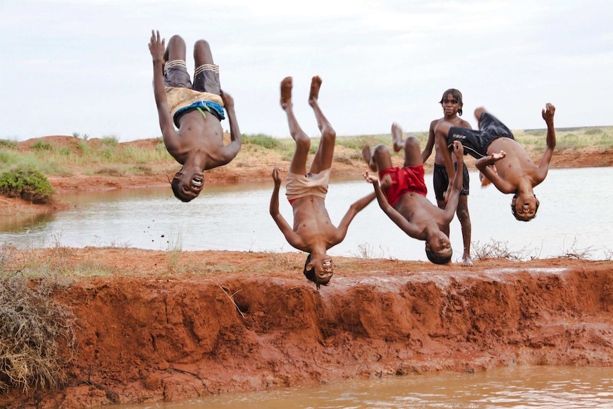 Four boys doing a backflip after swimming