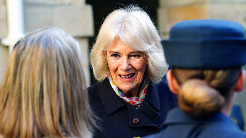 Queen Camilla smiles as she greets two women.