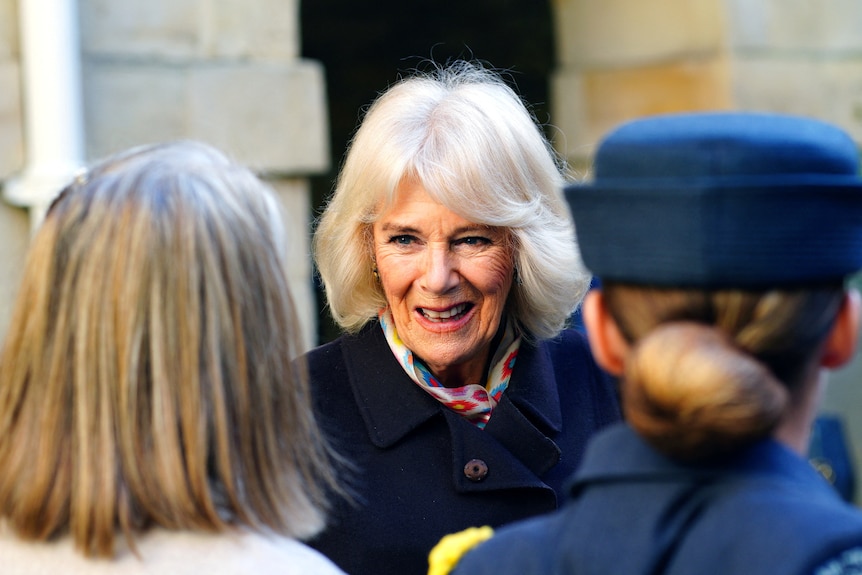 Queen Camilla smiles as she greets two women.