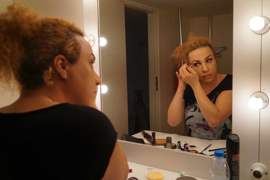 Transgender woman Seyhan Arman applies make-up to her face in a dressing-room mirror.