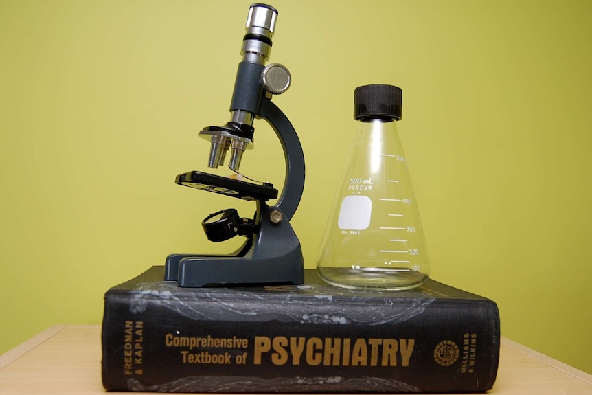 A large text book titled 'Psychiatry' sits on a table, with a microscope and beaker sitting on top.