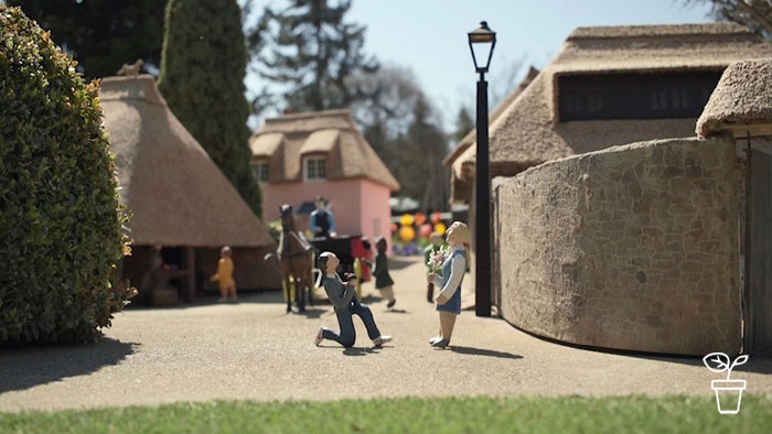 Miniature model village with male figurine on one knee proposing to female figurine