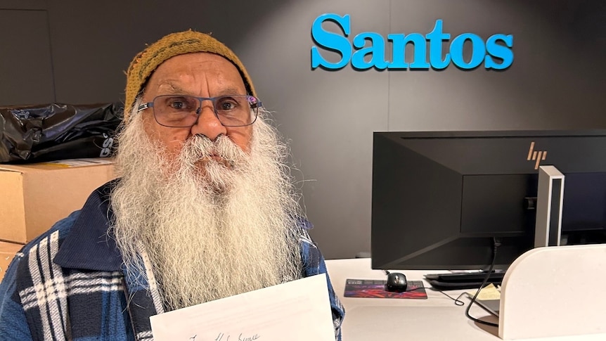Aboriginal elder Major 'Moogy' Sumner holds a letter near a Santos sign in an office.