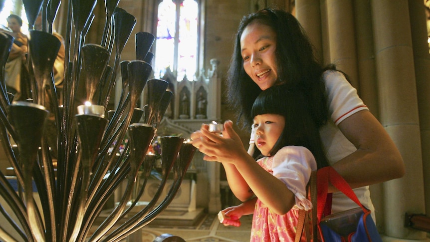 A woman and child of Chinese descent light a candle in church.