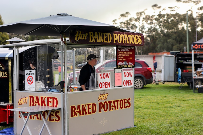 Man stands inside baked potato van with signage 